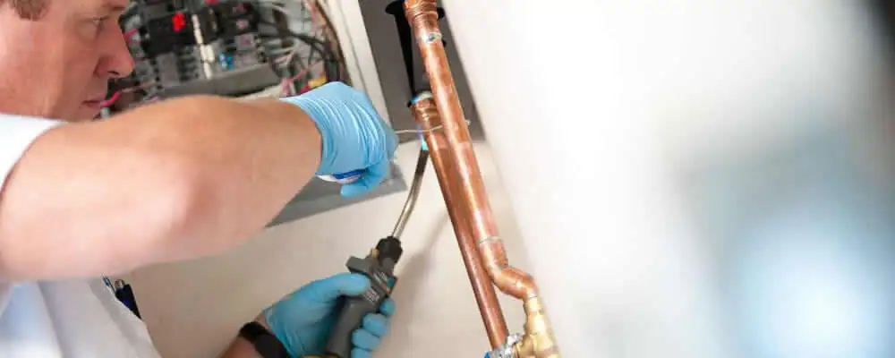 Water heater repair technician testing copper pipe connections and controls in Denver, CO